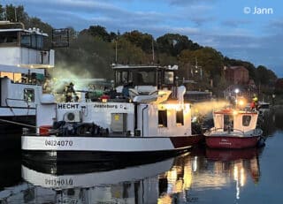 Zur Brandbekämpfung auf dem Binnenschiff "Hecht" gehen die Einsatzkräfte über einen Landungssteg und das Deck eines anderen Binnenschiffes sowie Feuerwehrschiff „Elbe I“ vor. Foto: Jann