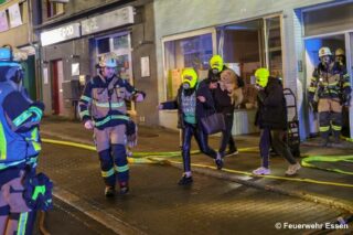 Feuerwehr und Bewohner mit Fluchthauben gehen aus Gebäude