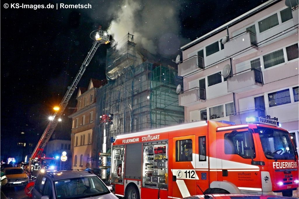 Eine Drehleiter im Einsatz an einem mehrstöckigen Wohnhaus mit rauchendem Dachstuhl, davor ein Löschfahrzeug der Feuerwehr Stuttgart.